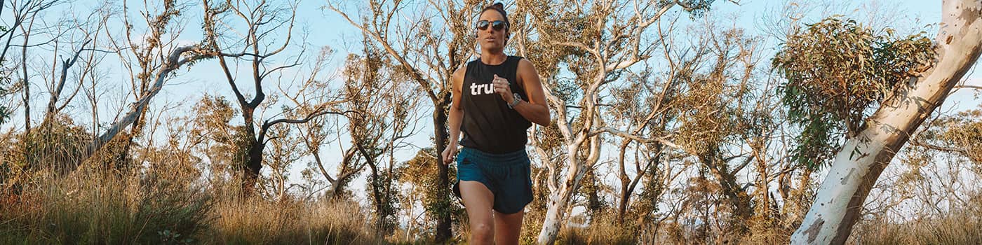 Person jogging on a sunlit dirt trail through eucalyptus woodland in the Australian bush — outdoor trail running and fitness banner.