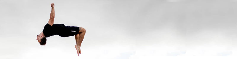 Athlete in black workout clothes performing a mid-air backflip outdoors against a cloudy sky — fitness acrobatics banner for workout, training, and healthy lifestyle.