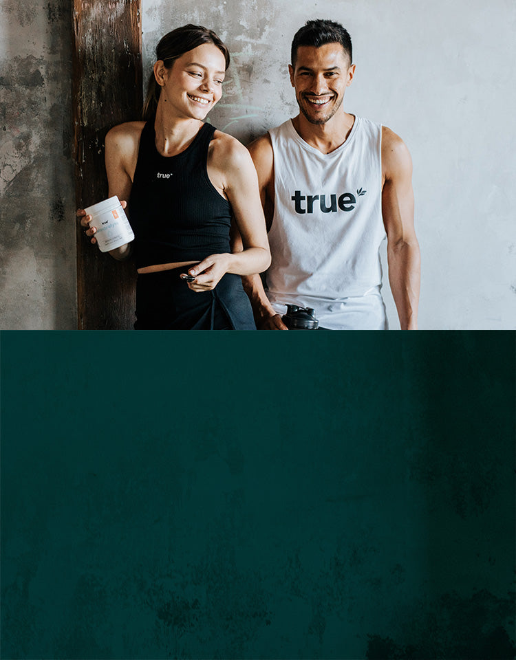 Smiling fit young man and woman wearing "true" activewear, woman holding a supplement jar and man holding a shaker bottle, leaning against a textured concrete wall — fitness supplements and lifestyle branding photo.