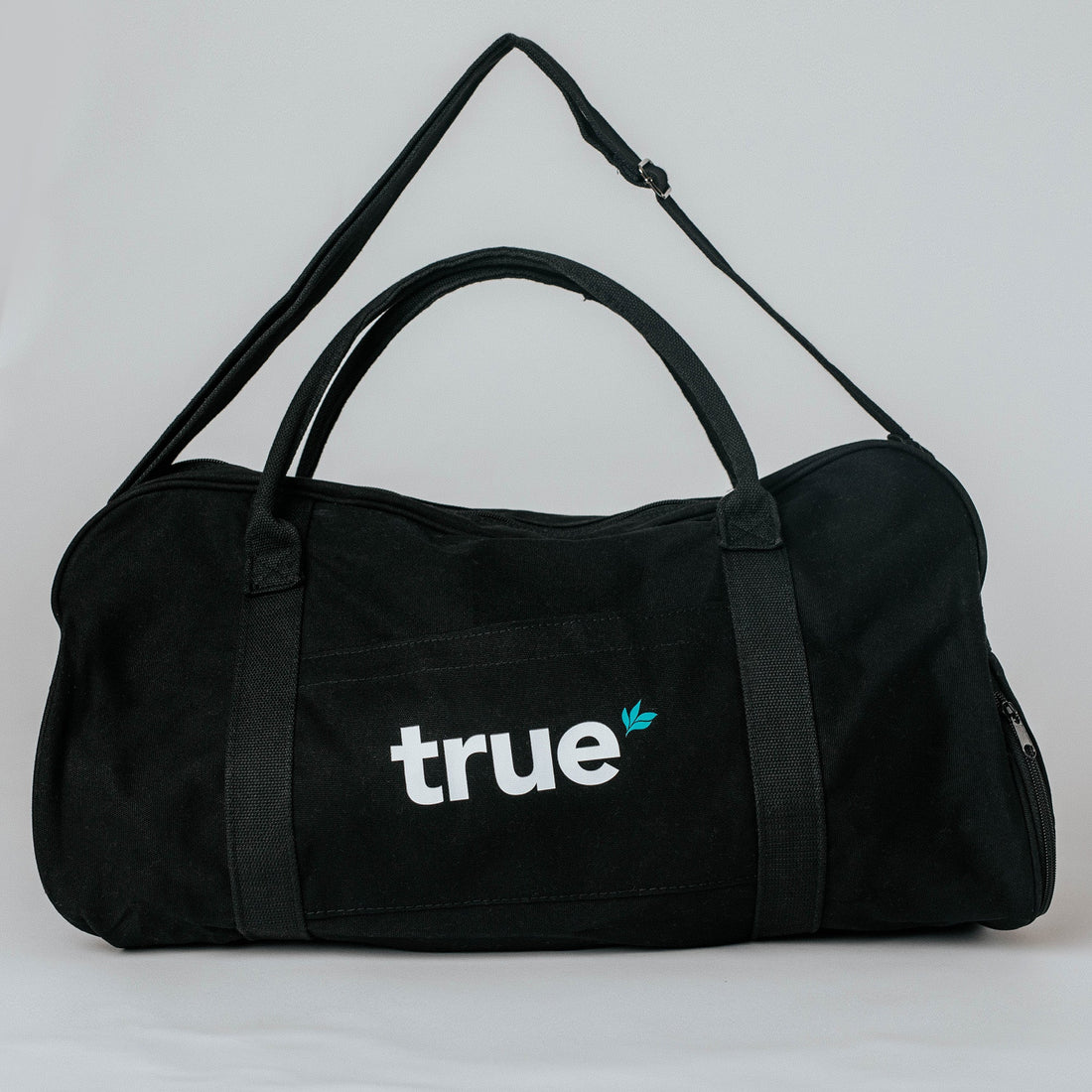 Black canvas medium duffel gym bag with white "true" logo and small teal leaf, adjustable shoulder strap and dual top handles — workout &amp; travel bag.