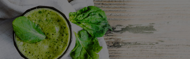 Top-down view of a green spinach smoothie in a black bowl with fresh spinach leaves on a white cloth and rustic wooden table — healthy lifestyle supplements banner