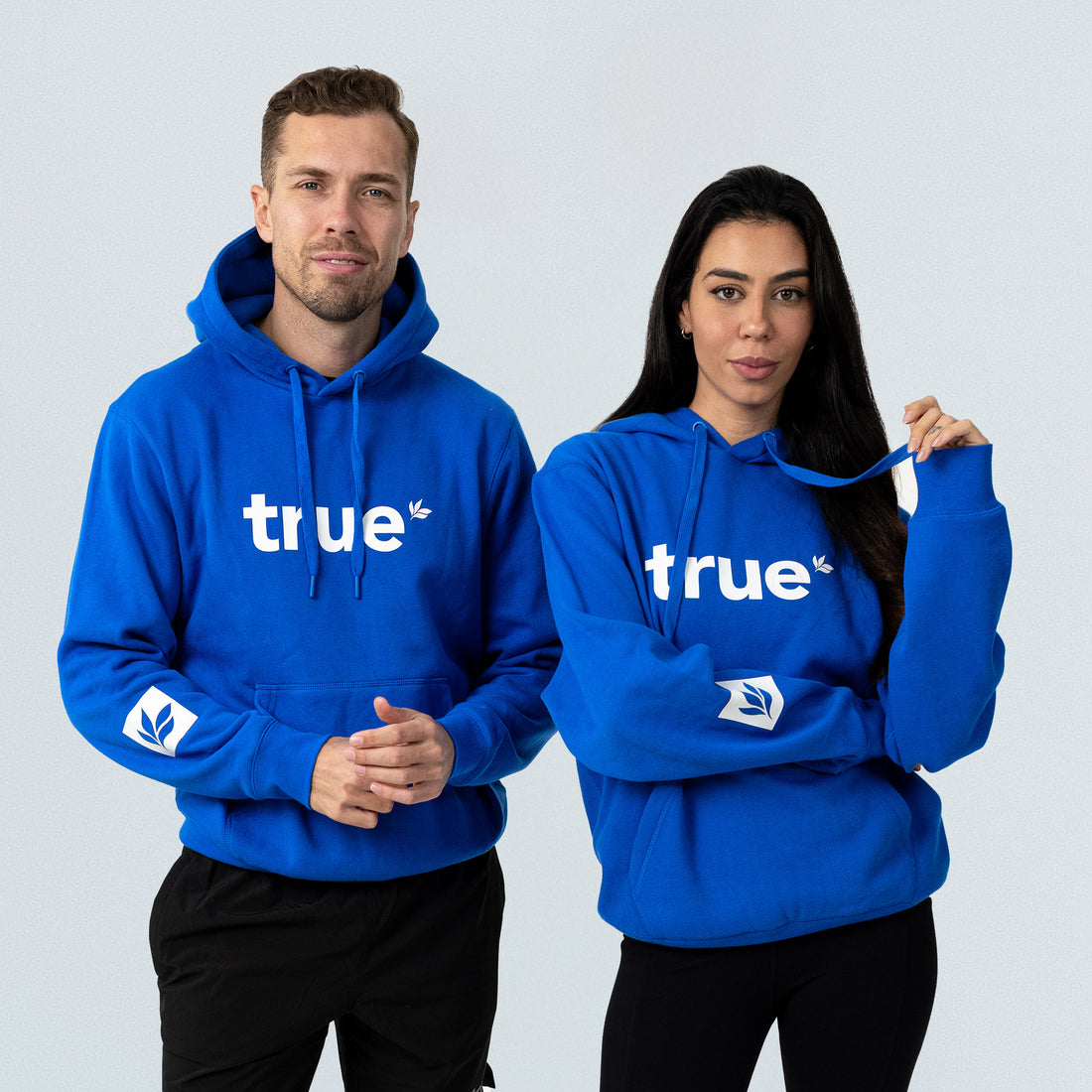 Royal blue unisex "true" logo hoodie on male and female models, front view product shot for ecommerce, casual streetwear apparel.
