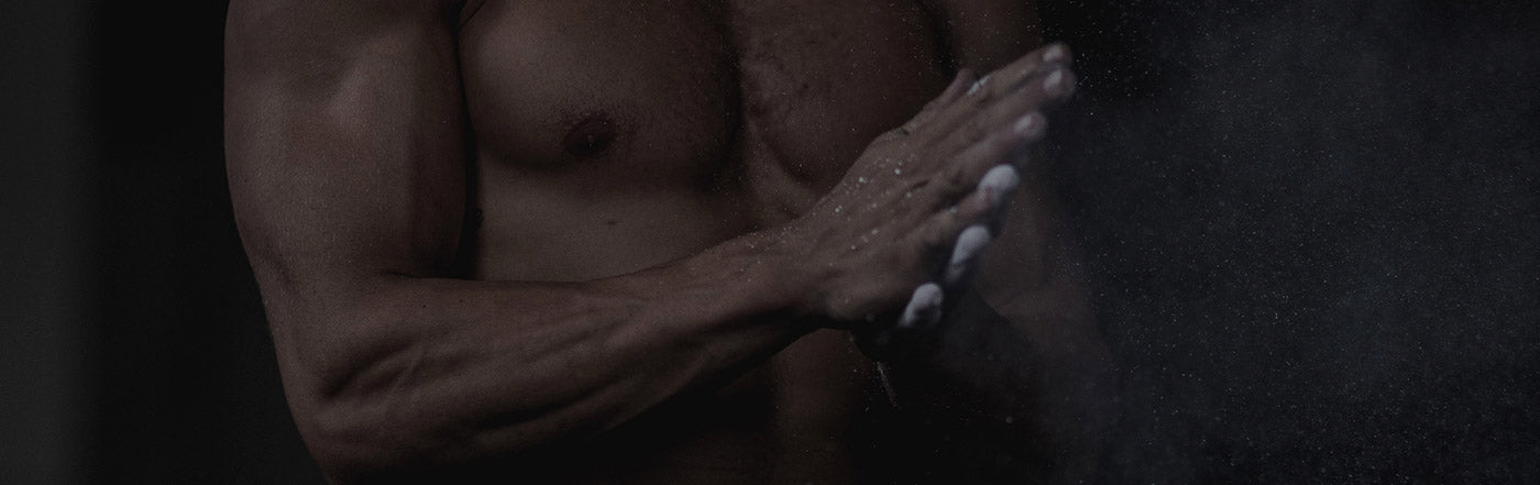 Shirtless muscular man rubbing chalk on his hands before weightlifting in a gym — fitness training, muscle gain, how to gain muscle.