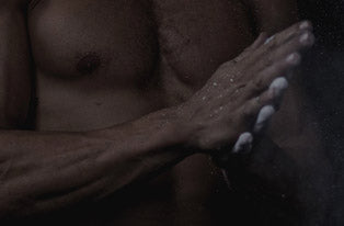 Shirtless muscular torso with hands applying moisturizer under water droplets — men's skincare/body lotion routine product image for grooming and muscle care.