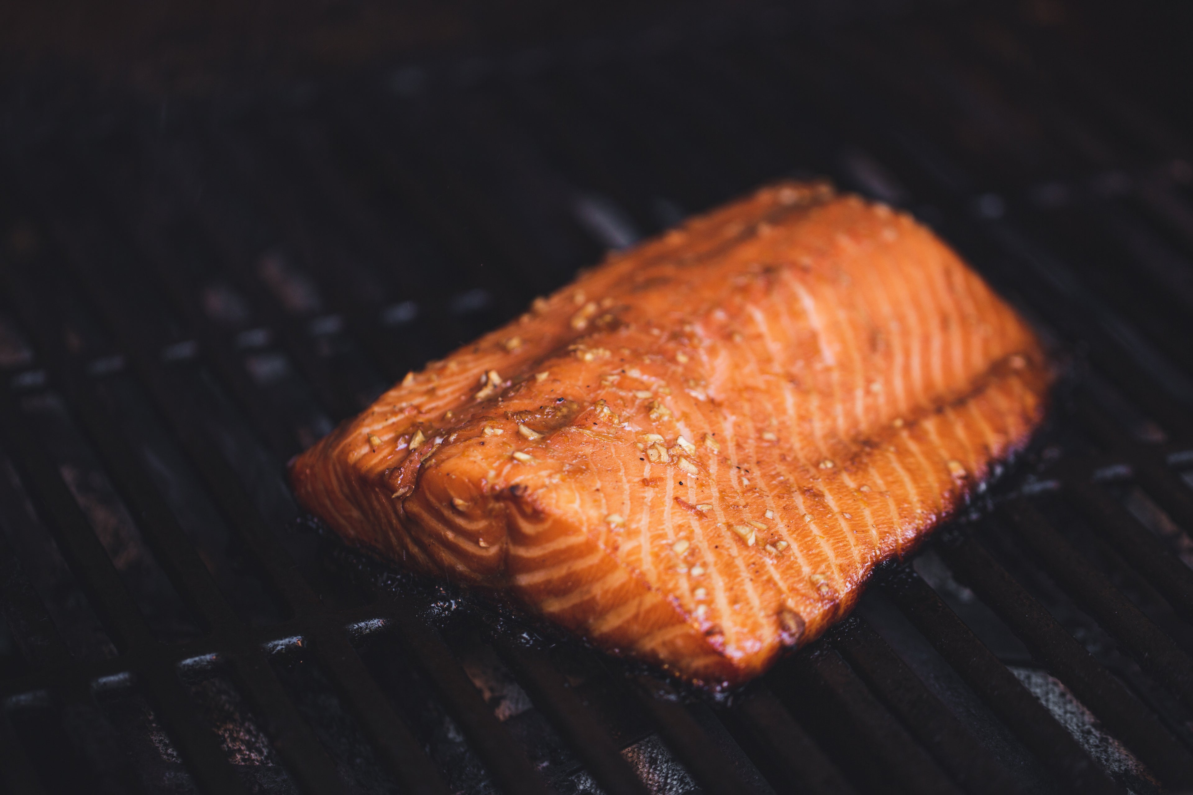 Close-up of a glazed, seasoned grilled salmon fillet cooking on a black charcoal grill — fresh seafood, healthy dinner idea, high-protein Pacific-style salmon dish.