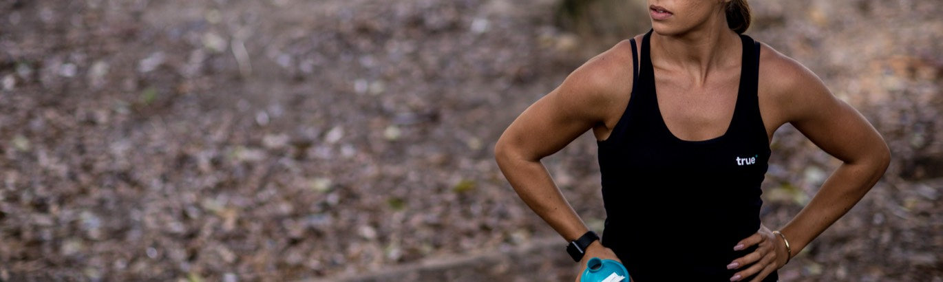 Woman in black tank top holding turquoise water bottle during outdoor workout in park with fallen leaves, fitness apparel product image.