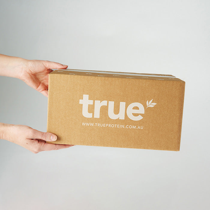 Hands holding a brown cardboard shipping box branded "true" with URL www.trueprotein.com.au — True Protein Australia package delivery.