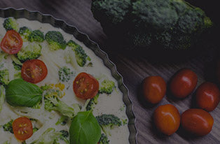 Woman's healthy broccoli and cherry tomato quiche in a tart pan on a wooden kitchen table with fresh broccoli and cherry tomatoes — healthy eating recipe, nutritious meal idea